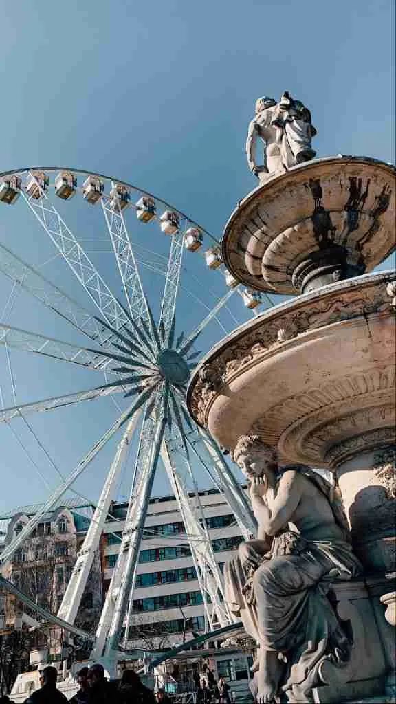 A large Ferris wheel in Budapest with a fountain in front of it 