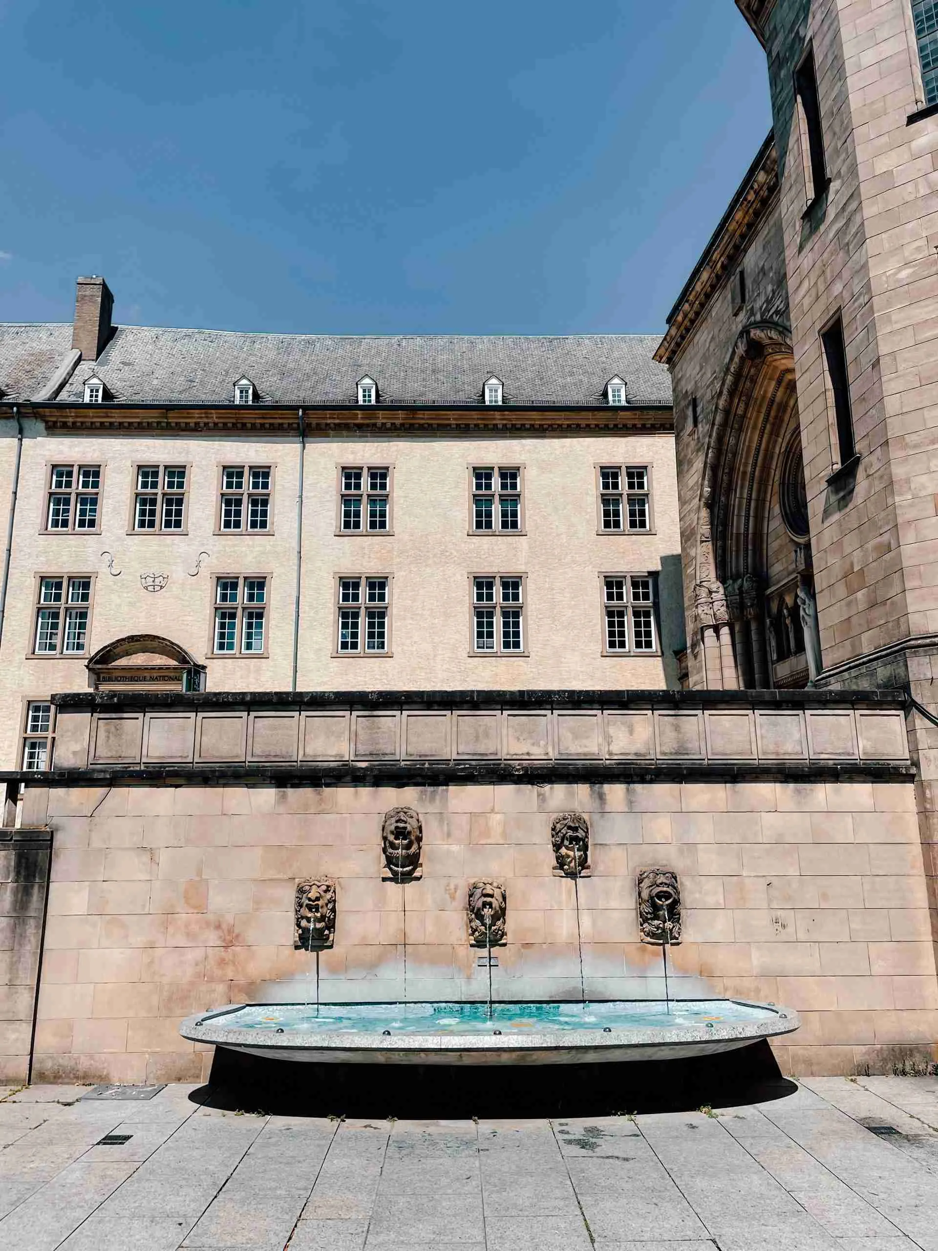 Stone figures with water pouring out of their mouths into a fountain - located on the side of the wall of the Luxembourg cathedral - Notre Dame