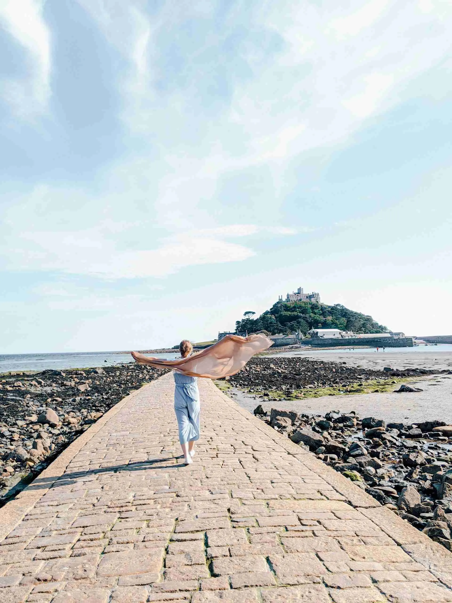 A girl walking towards the wind in St. Michaels Mount in Cornwall, her scarf blowing behind her. 