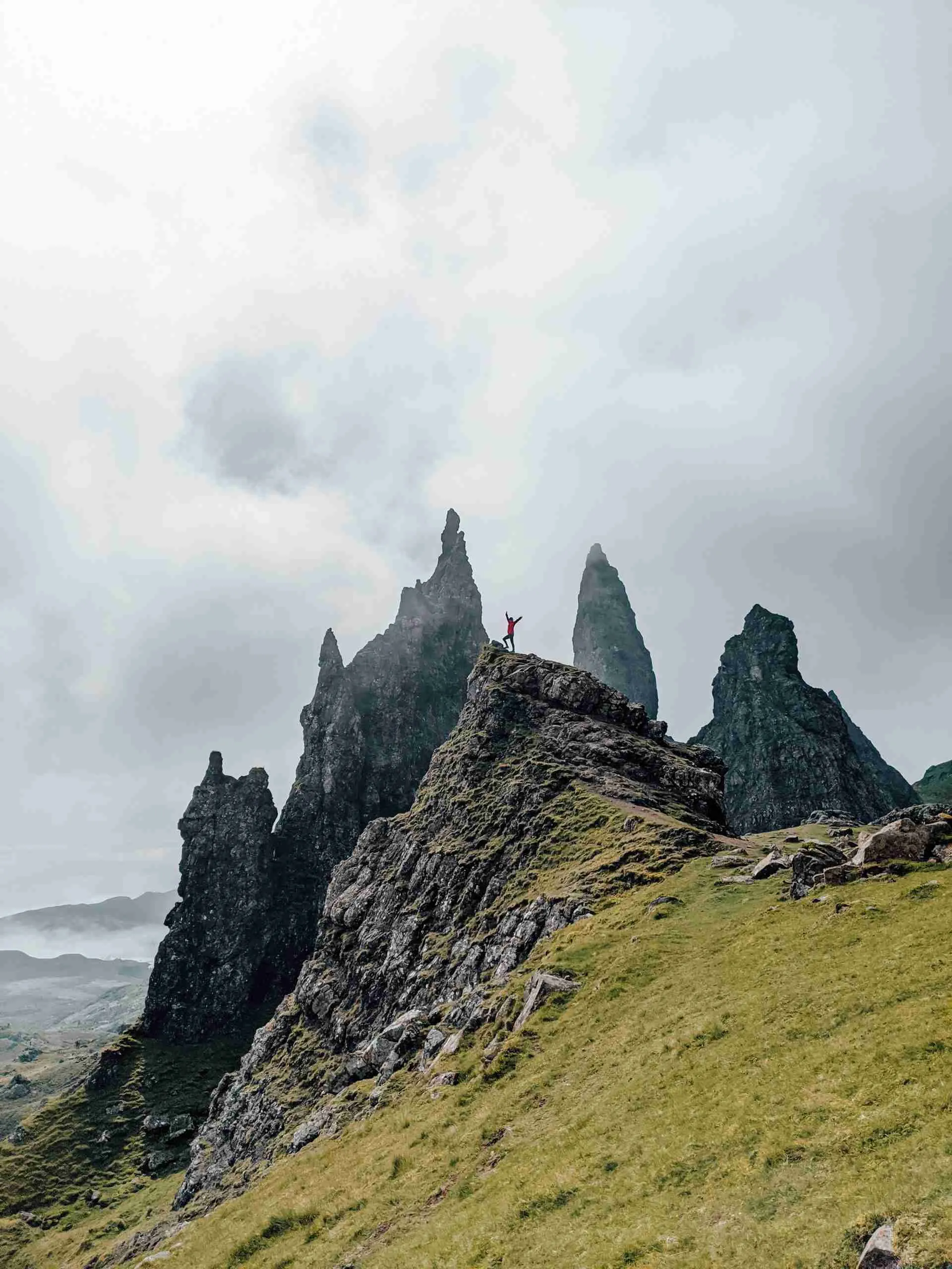 Someone standing on a rock on with the jagged peaks of the Old Man of Storr in the back ground