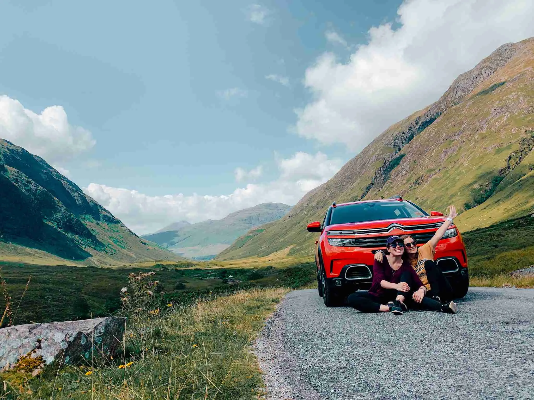 2 girls in the middle of the Scottish Highlands with their rental car ready for the UK road trip
