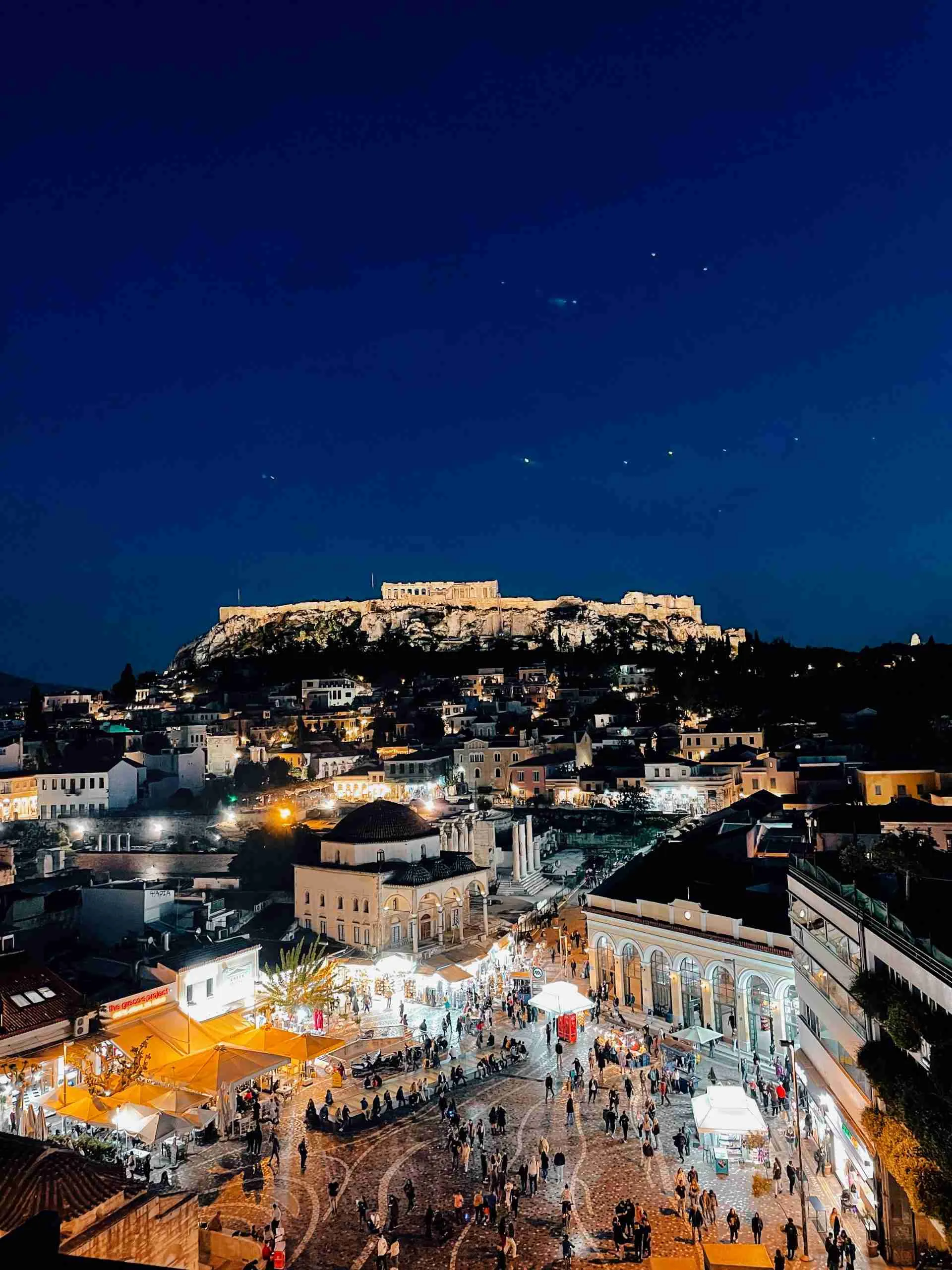 Athens at night overlooking the bustling city from a roof top bar with the Acropolis lit up in the distance