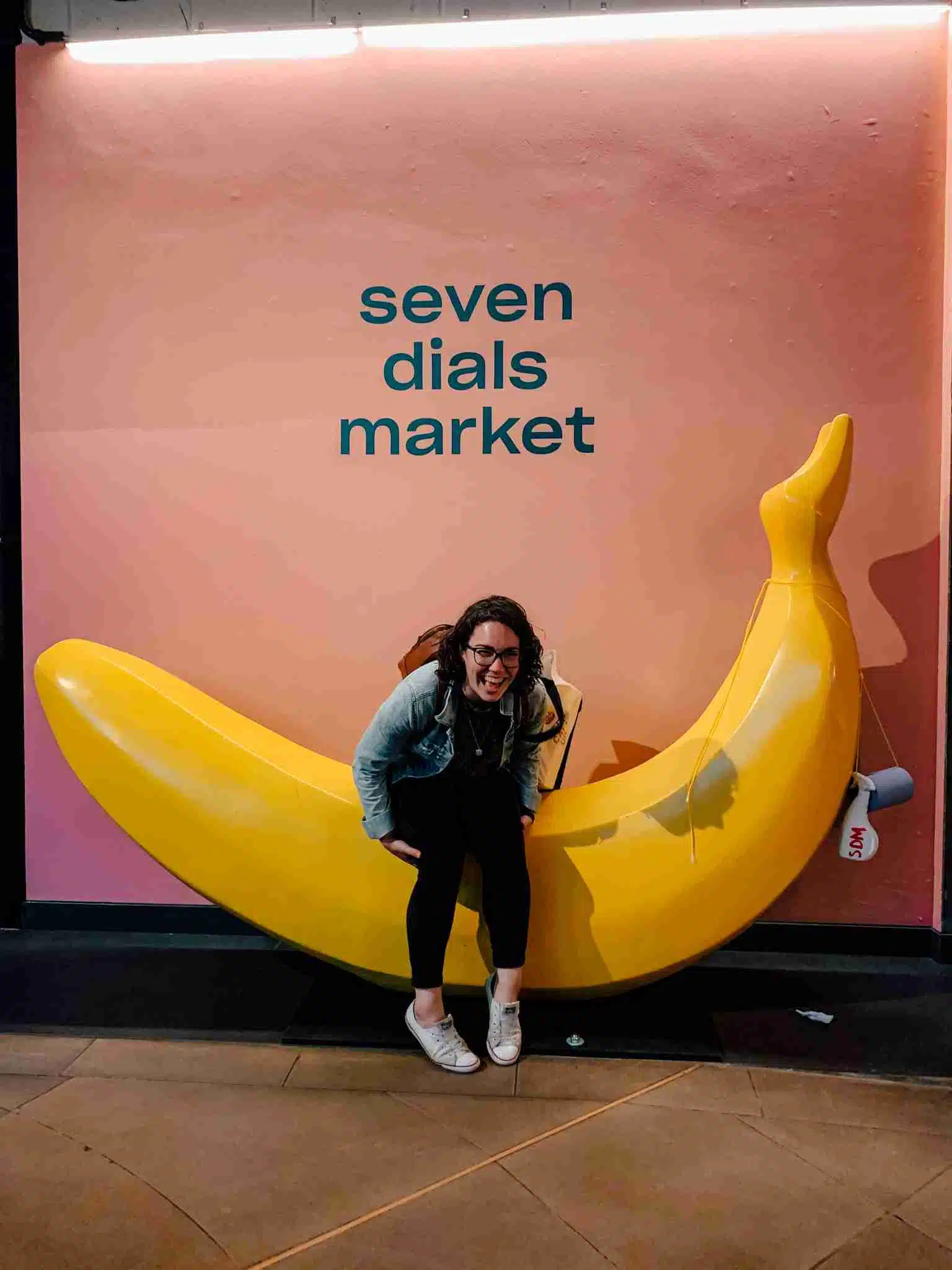 A girl sitting on a giant banana in Seven Dials Market 