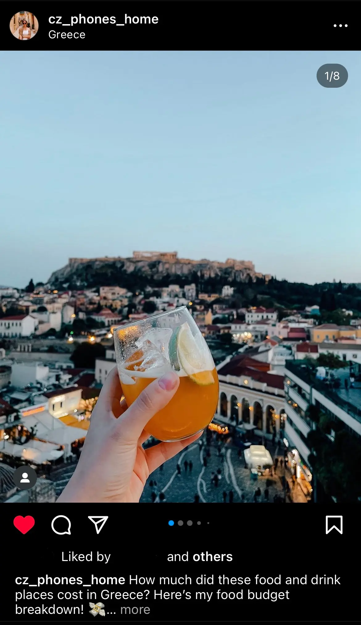 A screenshot of an instagram post of someone holding a cocktail in front of the camera with the acropolis sitting in the distance 