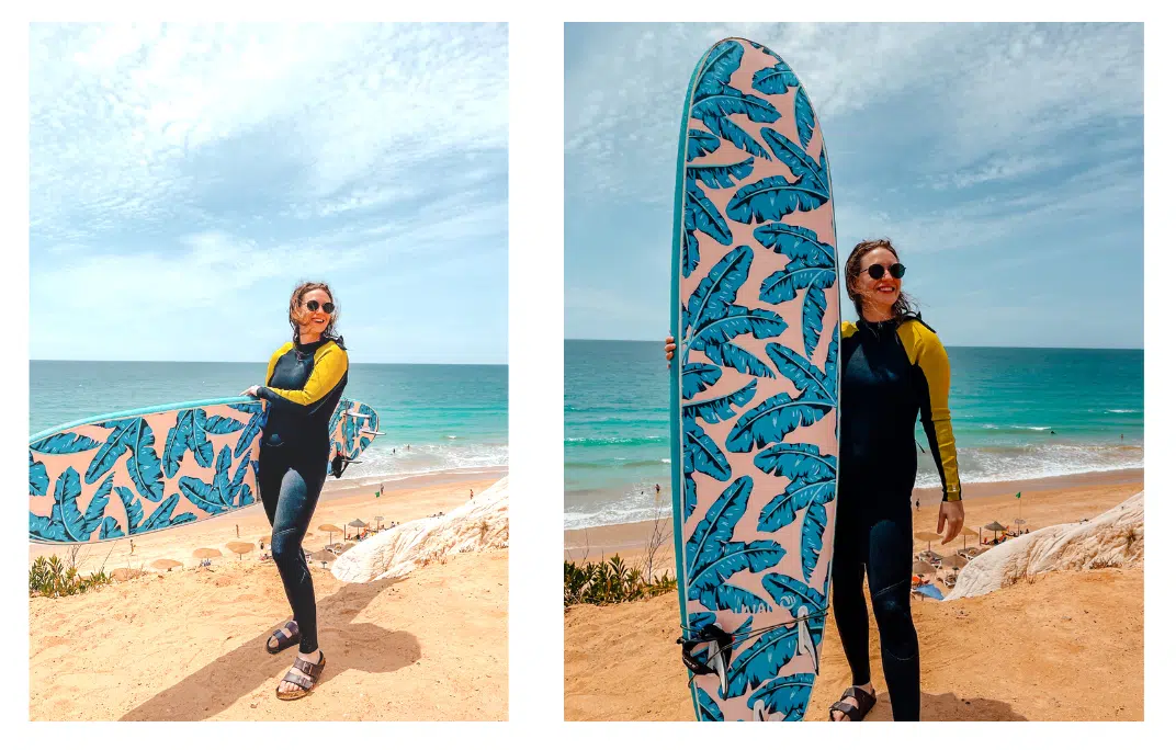 A girl standing in a wetsuit with a bright blue ocean and Algarve beach behind her holding a surf board, her hair blowing in the wind.