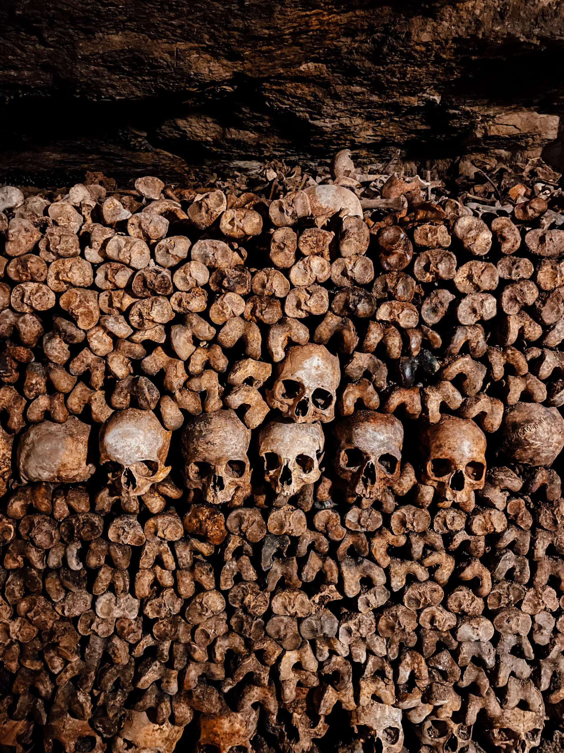 Inside of the catacombs of Paris - a series of skulls and bones sit staked on top of each other 