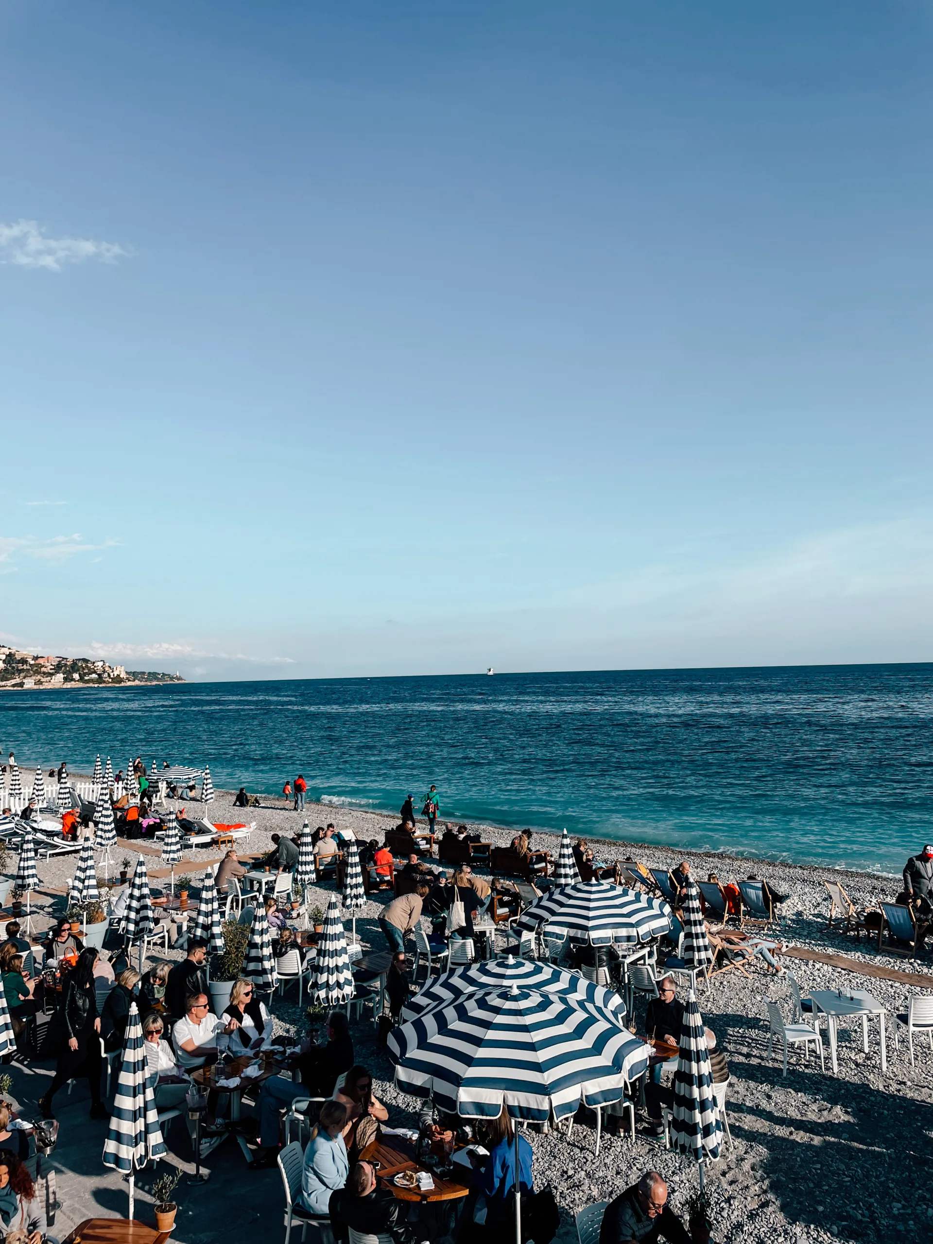The beach in Nice covered with blue and white umbrellas and people enjoying a cloudless day 