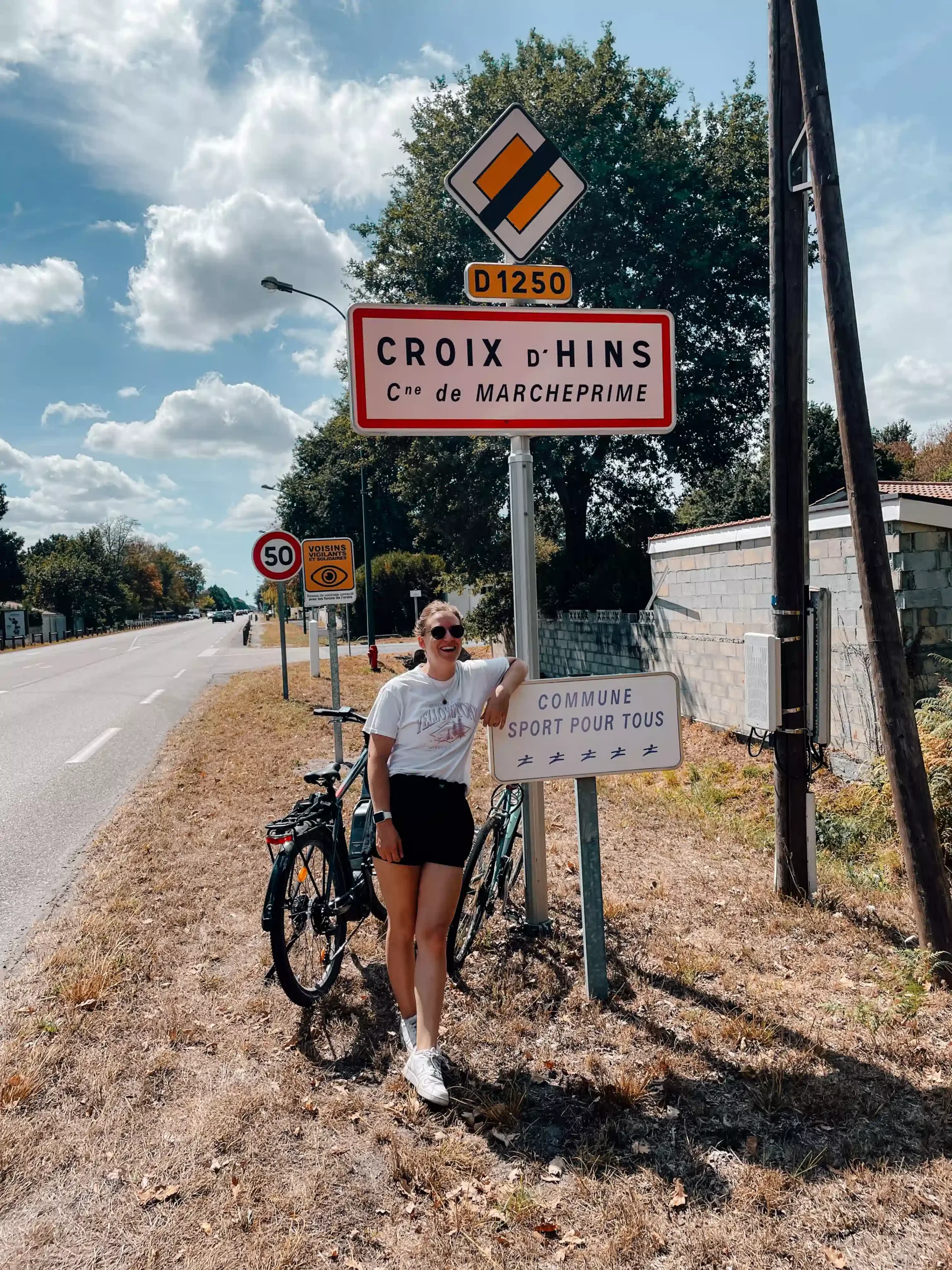 A girl stands with 2 bikes behind her with her arm on a road sign 
