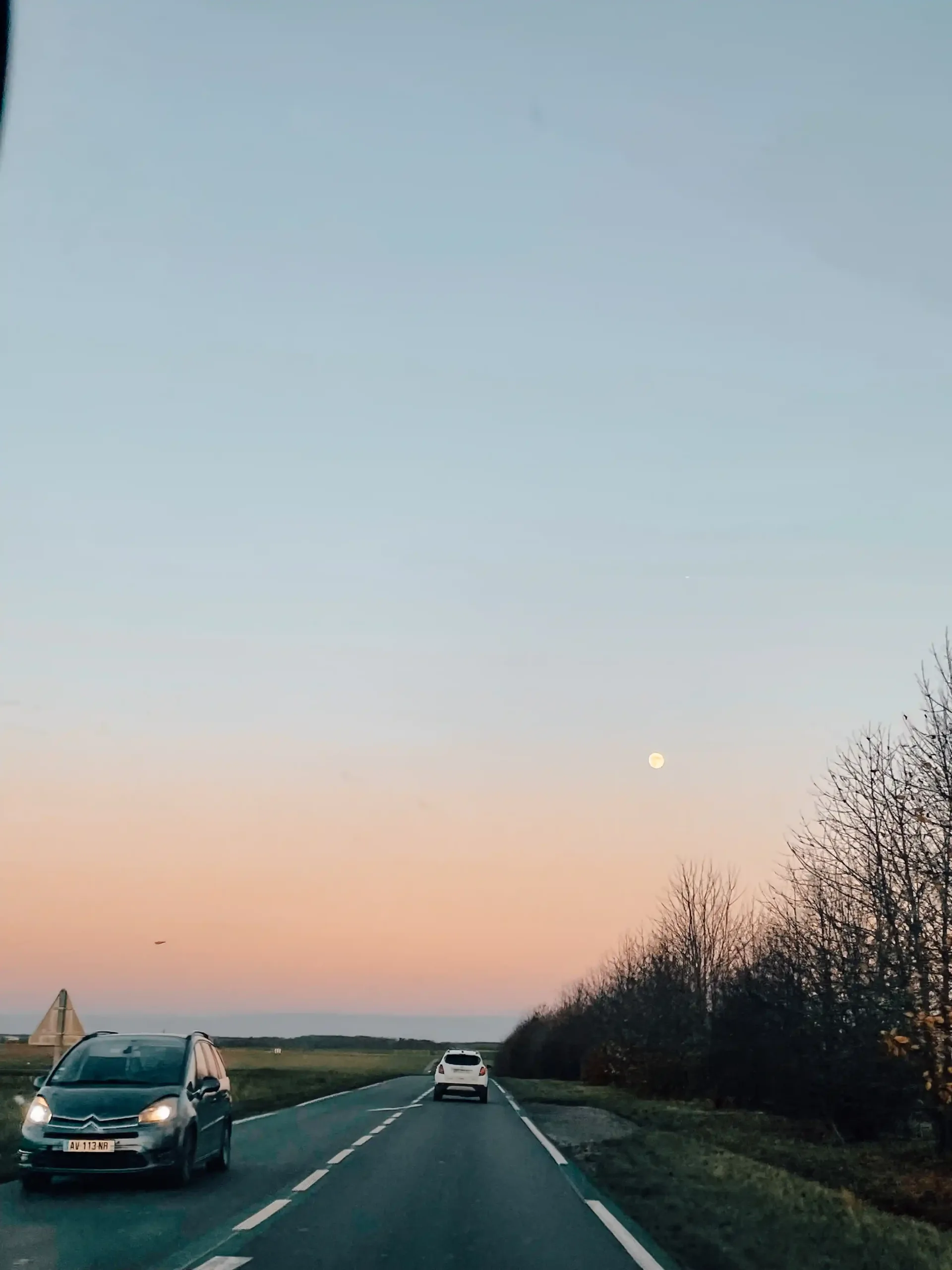 A long road with the moon in top right corner of the sky 