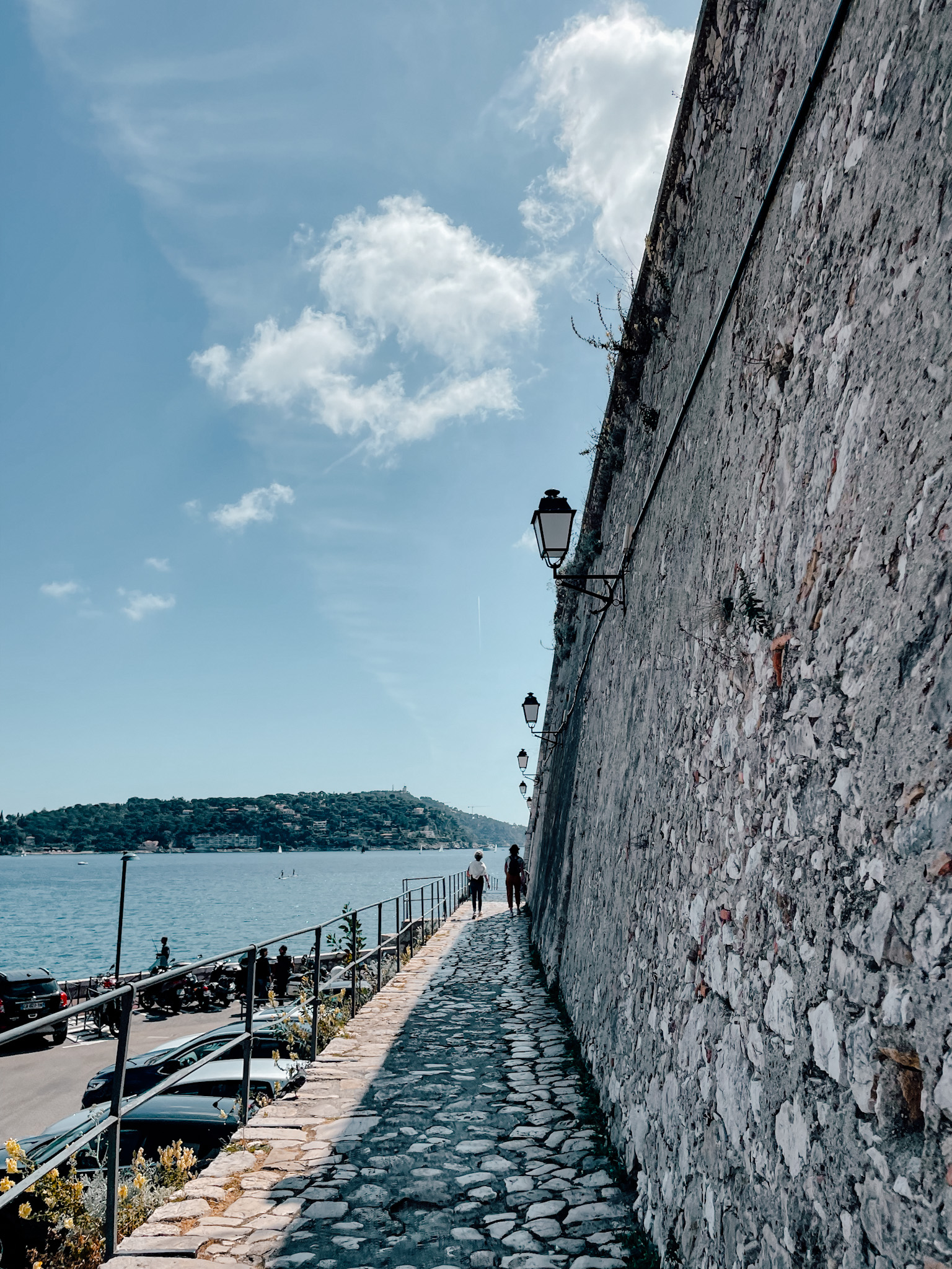 On the right stands a large stone wall next to a stone walk way which leads towards the sea - these are the walls of the old citadel in Villefranche-sur-Mer