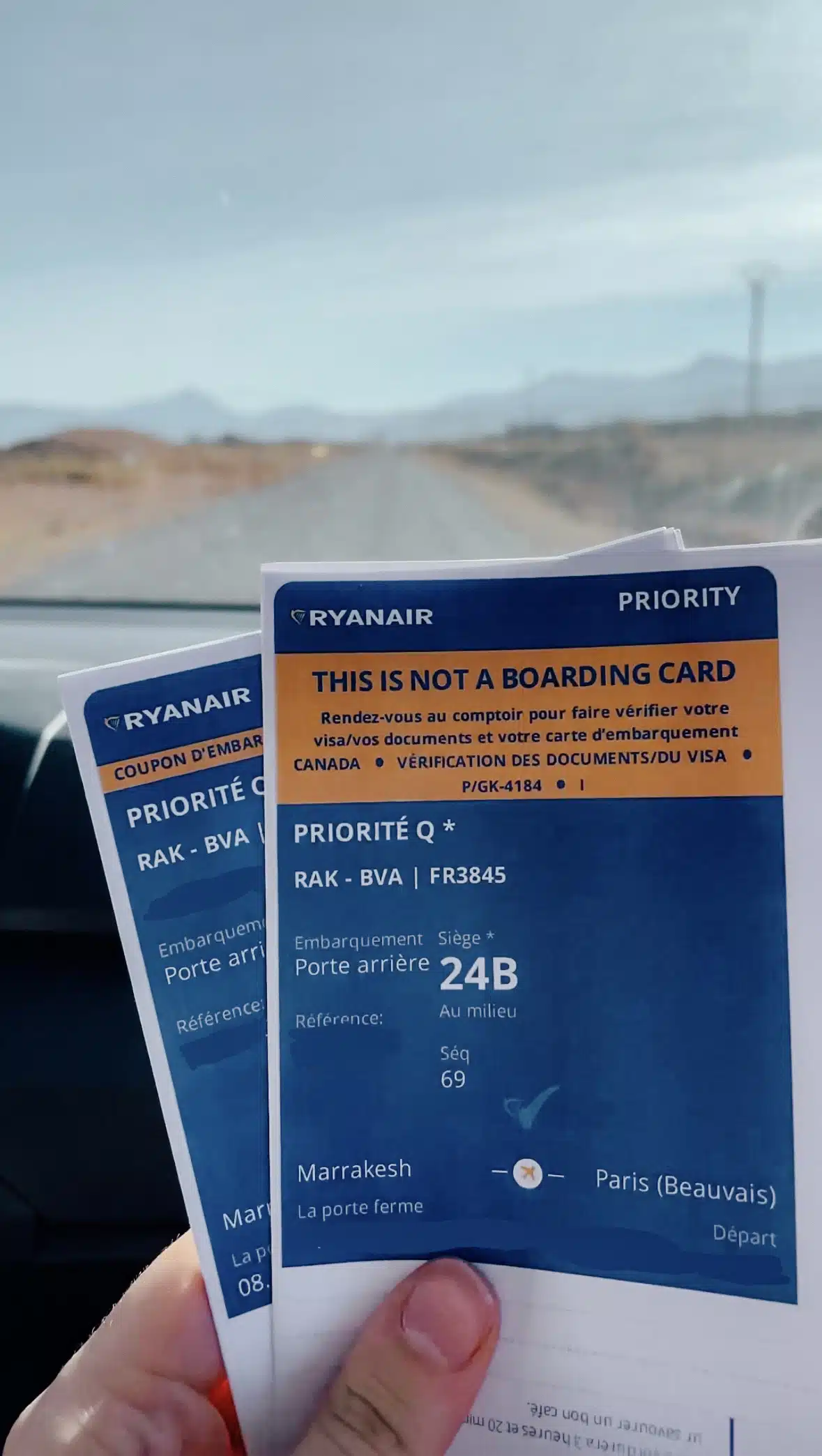 Someone holds a printed copy of their boarding pass in the car with a long road in front of them and a slight shadow of mountains in the distance