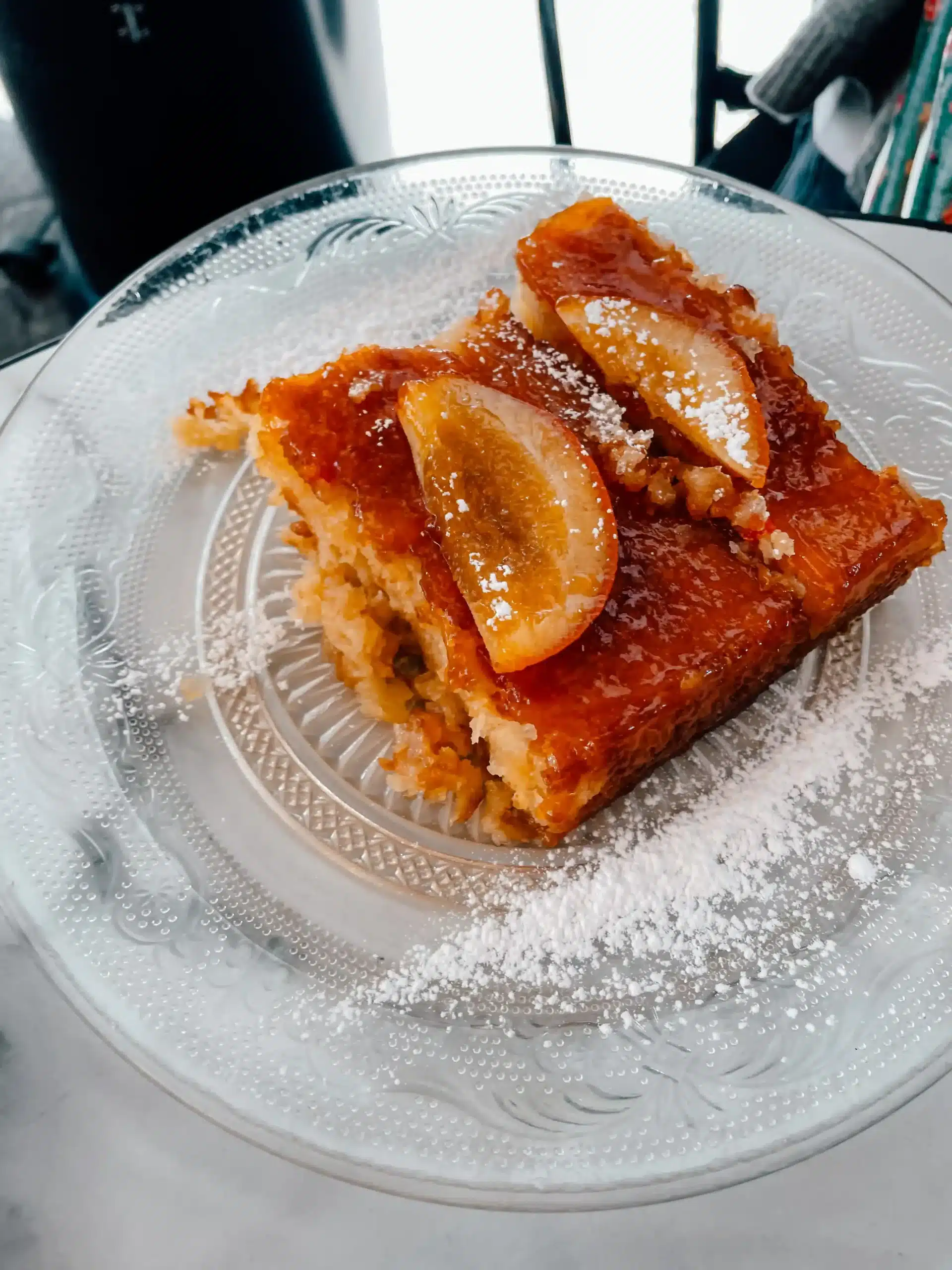 Greek orange cake, Portokalopita, sits on a glass plate with sprinkled powdered sugar on top 