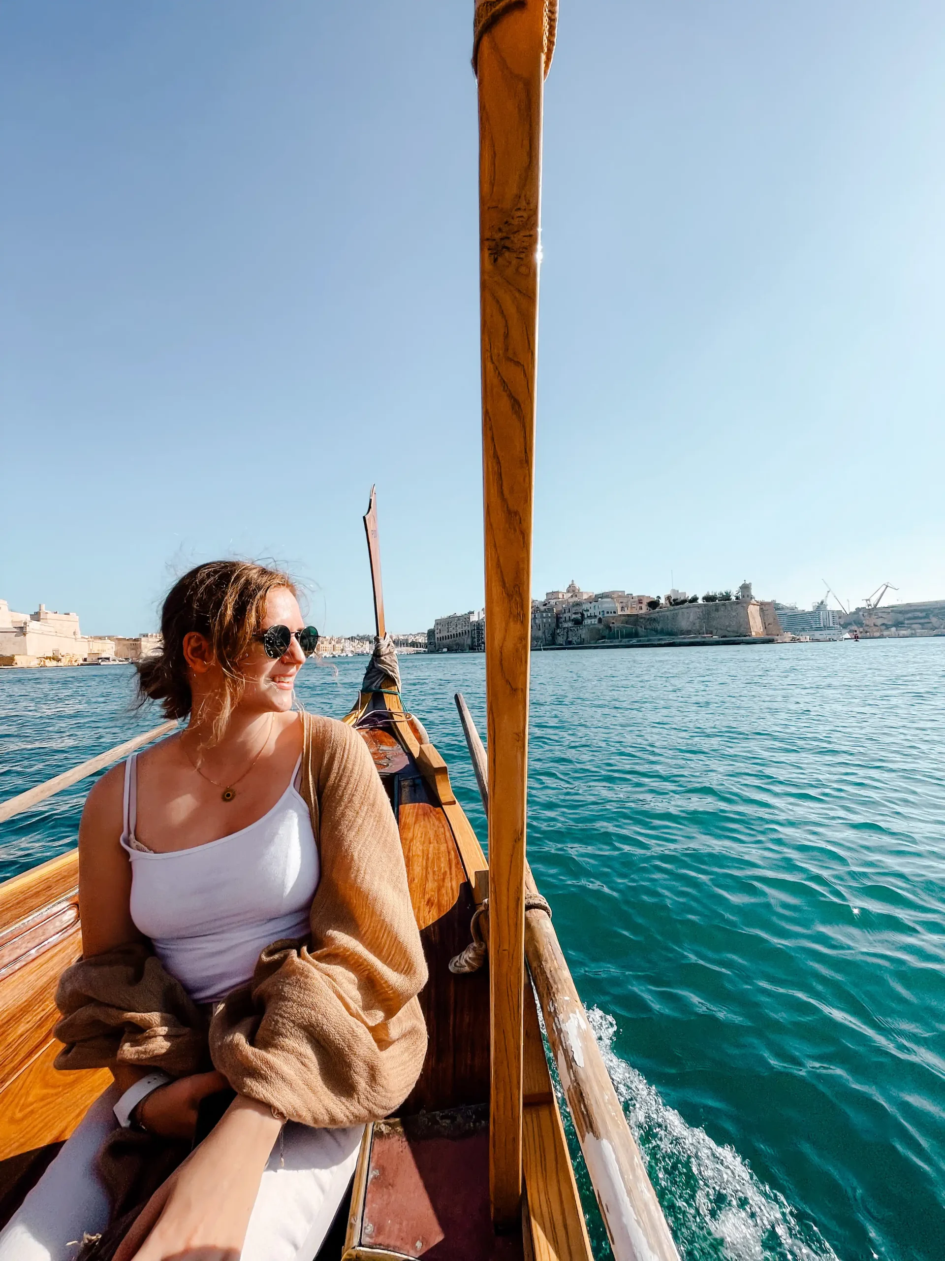 girl looking out at the water while riding a Maltese boat with the city on the horizon