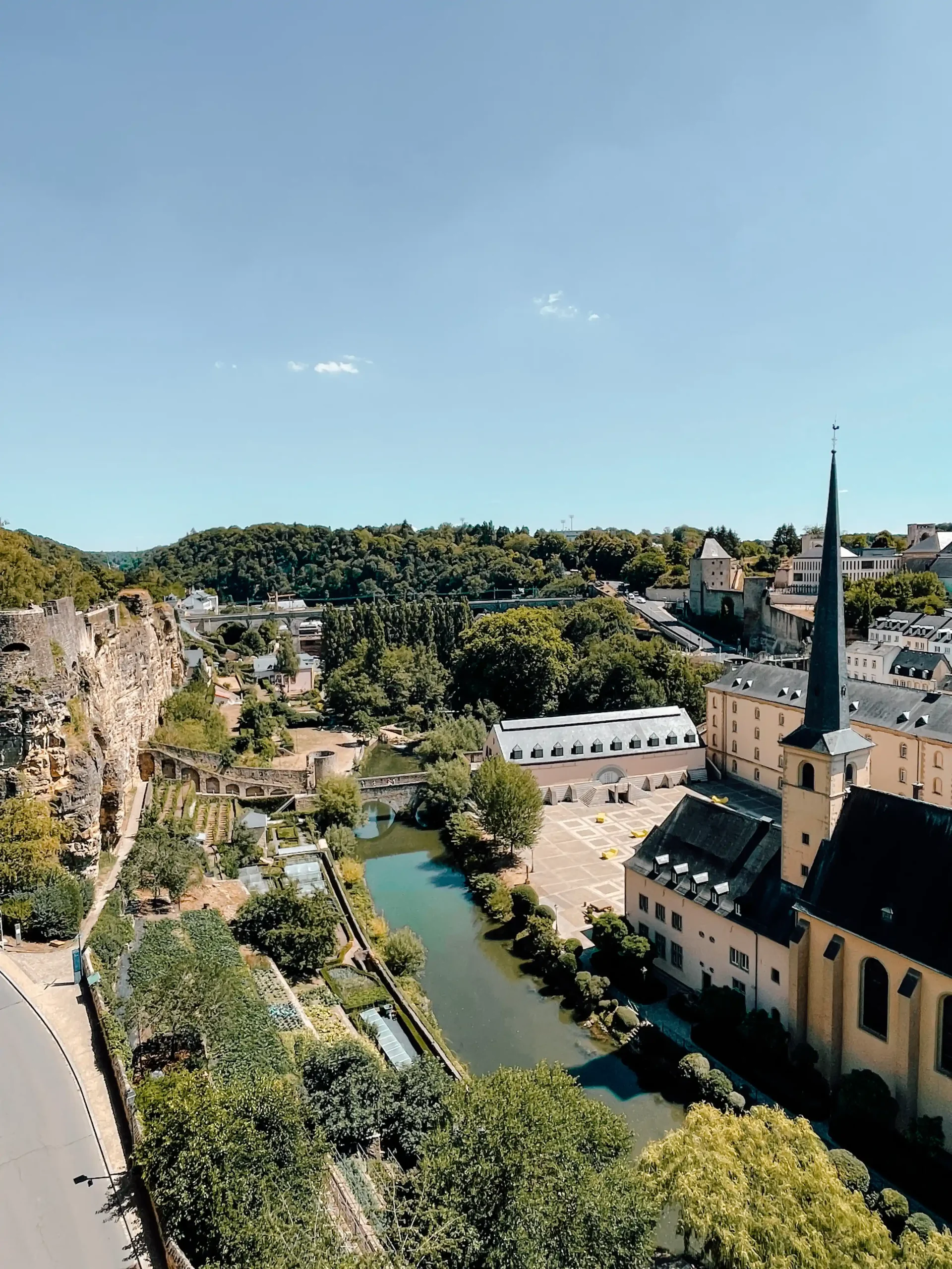 View overlooking the Lower City of Luxembourg with a building with a tall steeple standing in the front beside a river and a bridge in the far distance