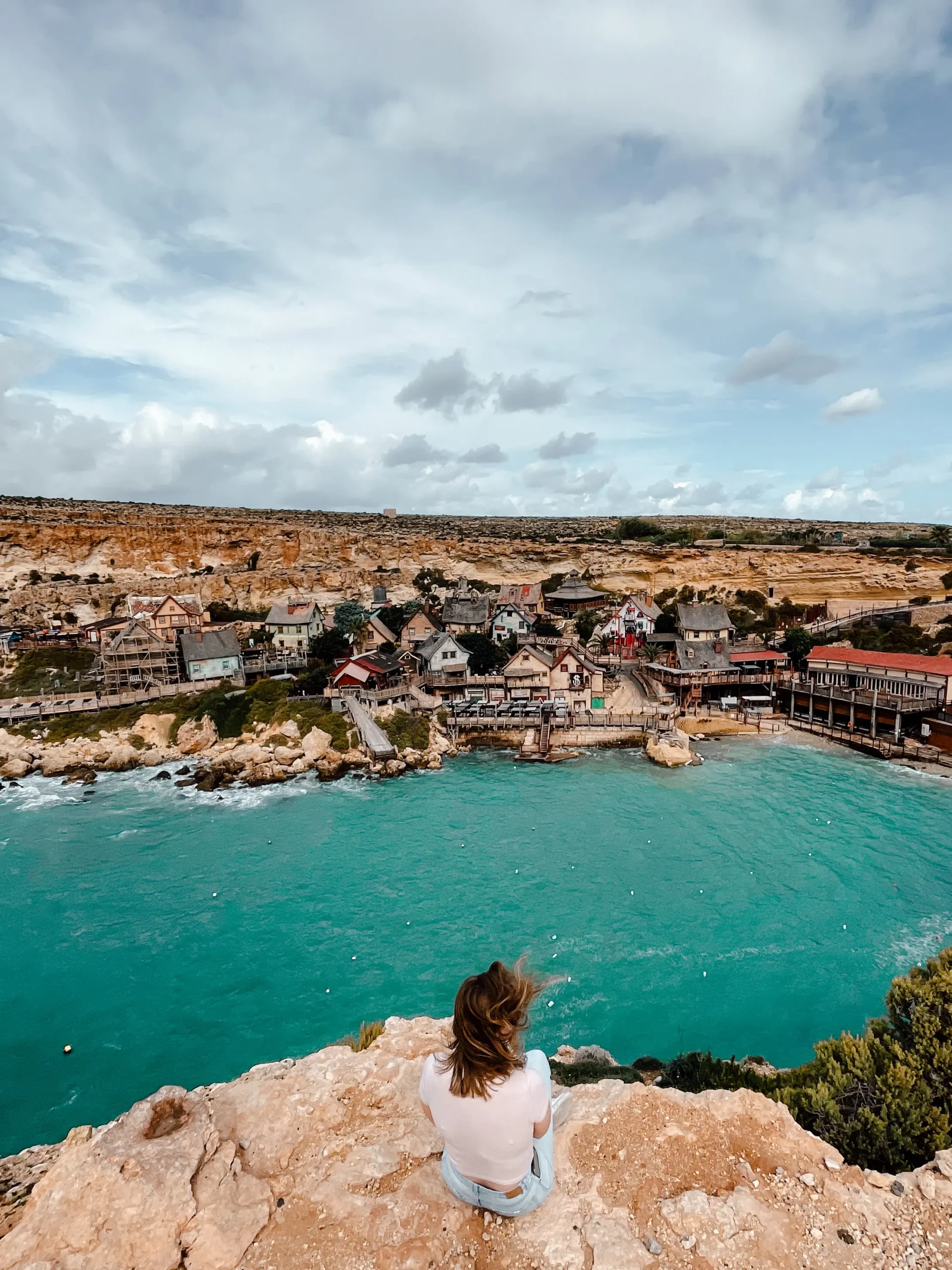 A girl sits on a rocky edge looking out at Popeyes village 